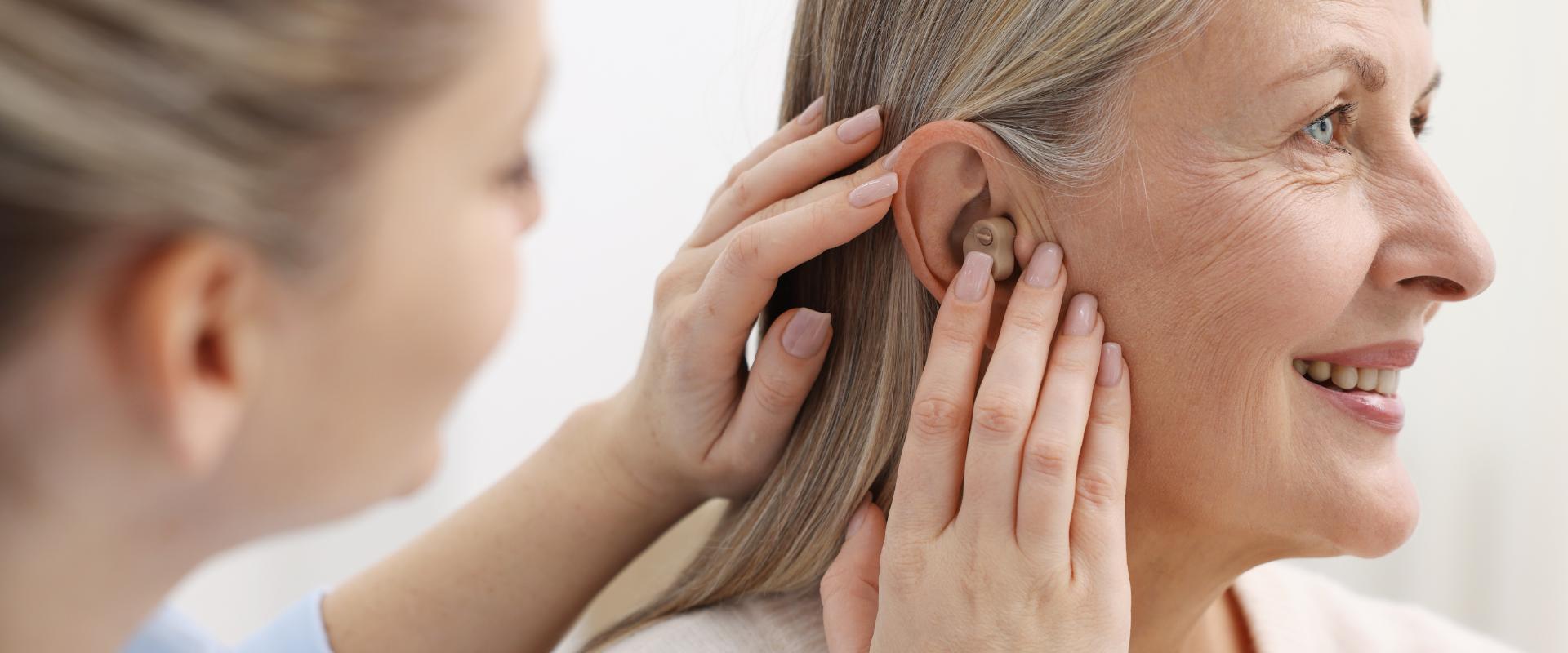 Fonoaudióloga adaptando um aparelho auditivo intracanal discreto na orelha de um paciente sorridente, consultório clínico bem iluminado, foco no encaixe delicado do dispositivo, fotografia realista