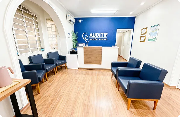 Fonoaudióloga sorridente ajustando aparelho auditivo atrás da orelha de paciente idosa em consultório claro e moderno, tons de azul e branco, luz natural, fotografia realista profissional