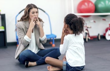 Adult female therapist guiding young girl in speech therapy